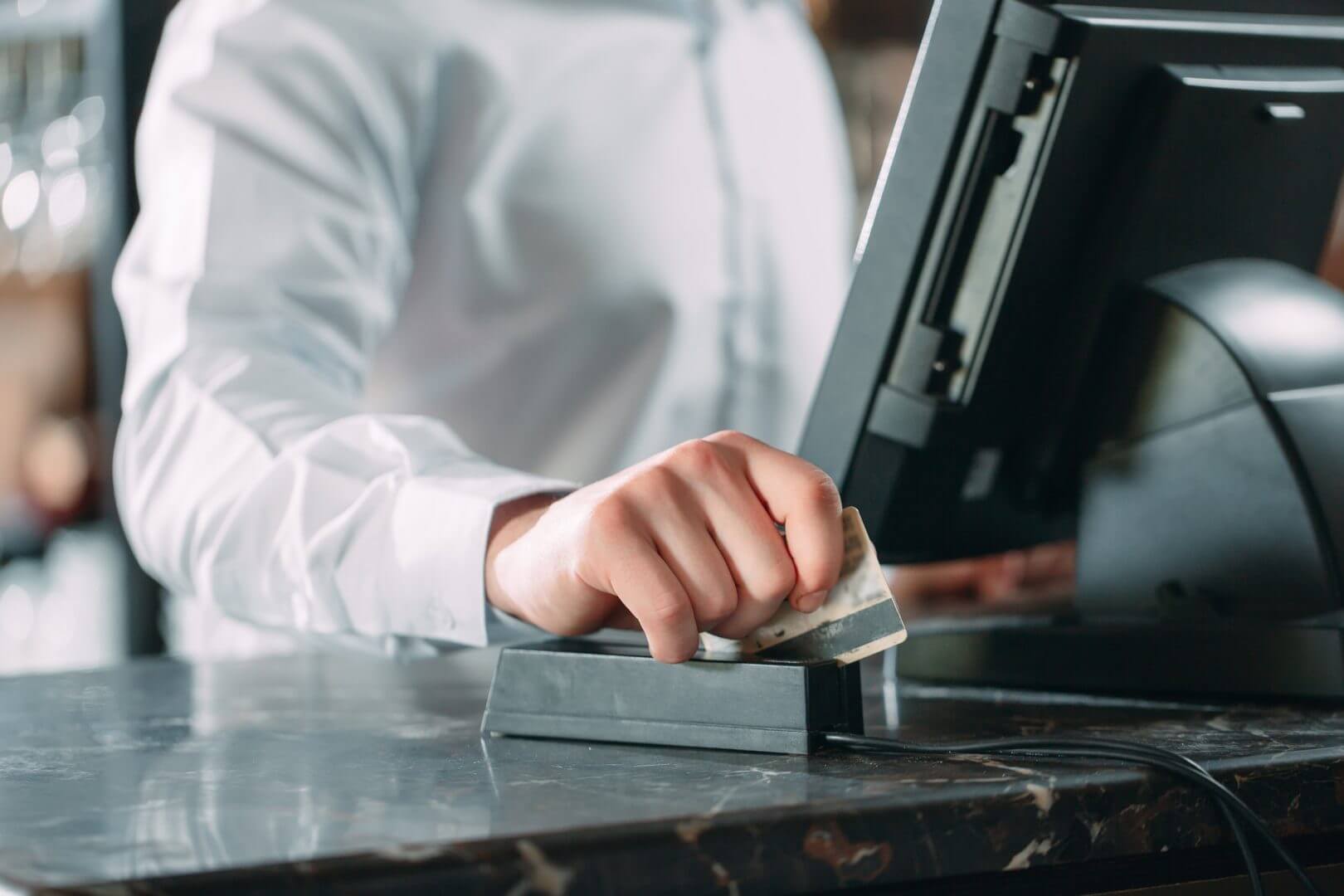 small business, people and service concept – happy man or waiter in apron at counter with cashbox working at bar or coffee shop. restaurant pos system
