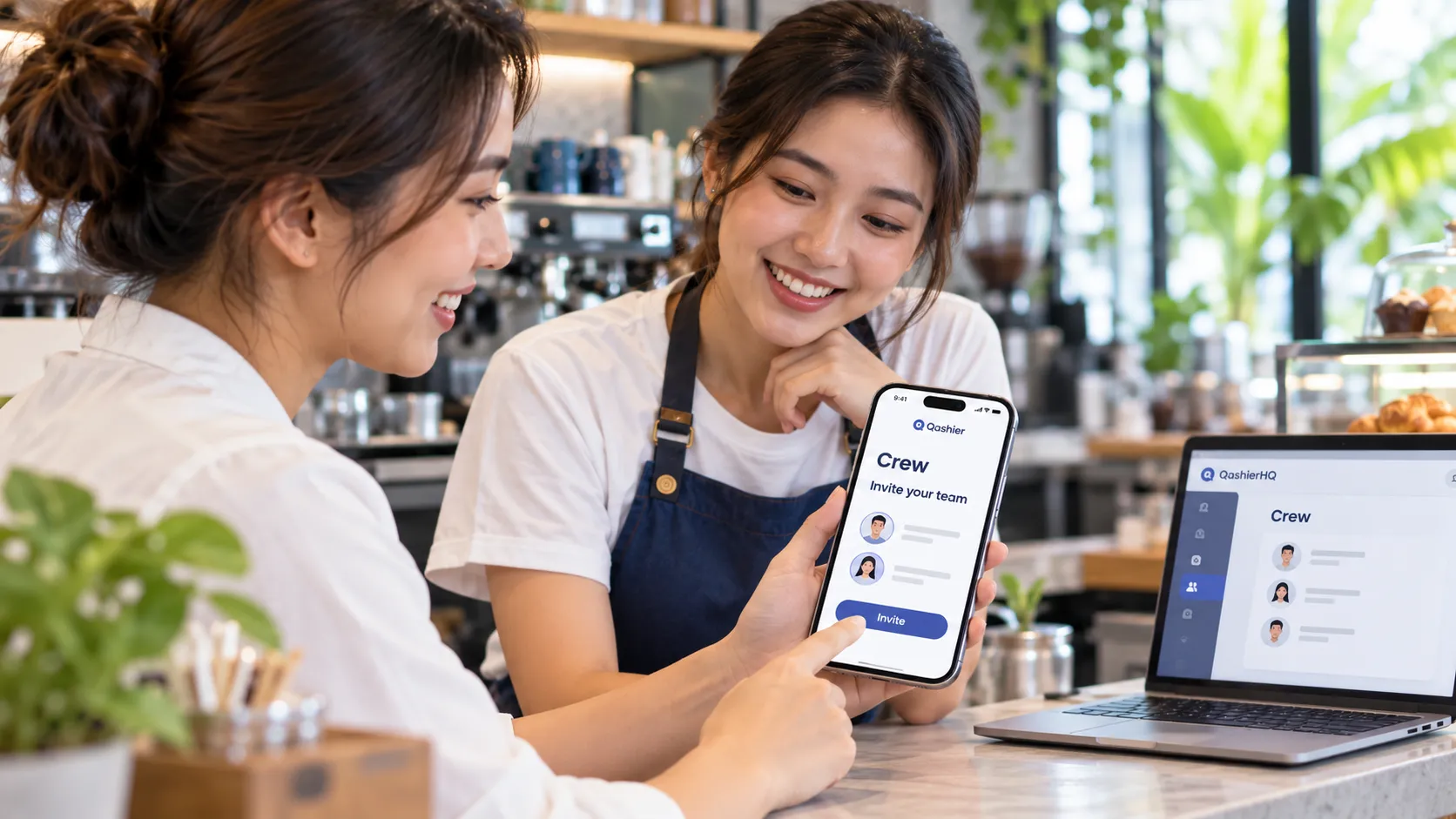 พนักงานร้านกาแฟสองคนยิ้มให้หน้าจอเชิญเข้า Crew ในแอป Qashier โดยมี Crew เปิดอยู่ใน QashierHQ บนแล็ปท็อปข้างๆ