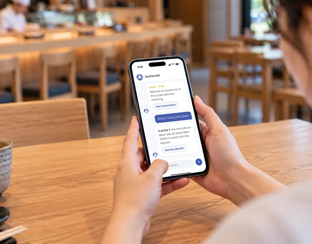 A restaurant owner checks QashierGM on her phone at a table in her Japanese restaurant